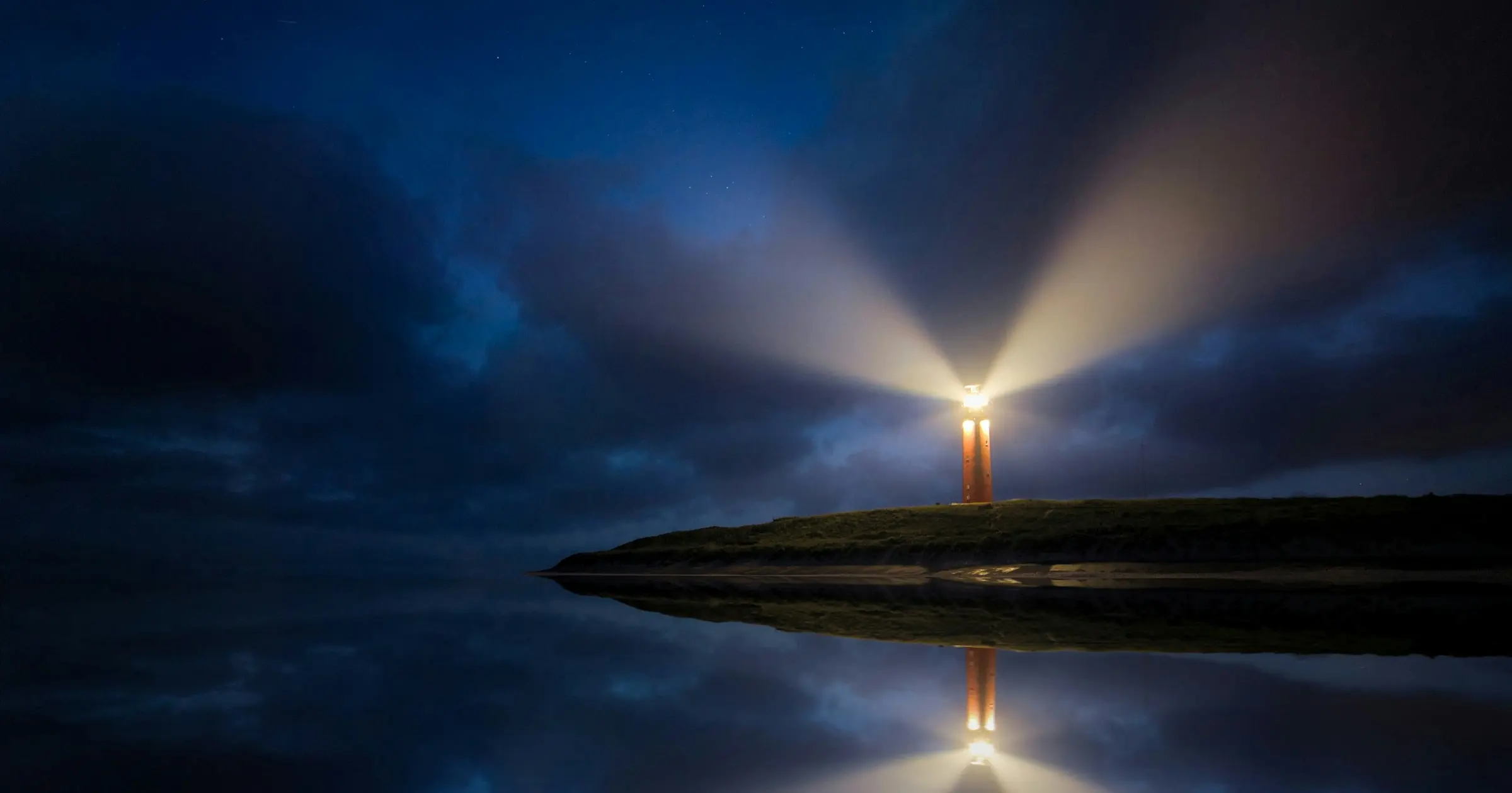 Lighthouse sweeping beams of light across a dark night sky over still water