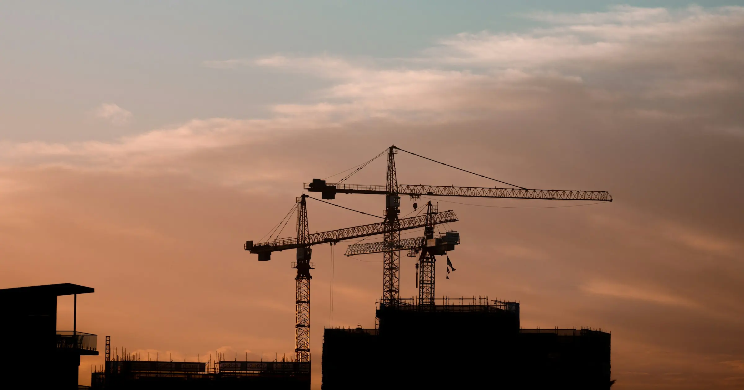 Tower cranes silhouetted over a building under construction at sunset