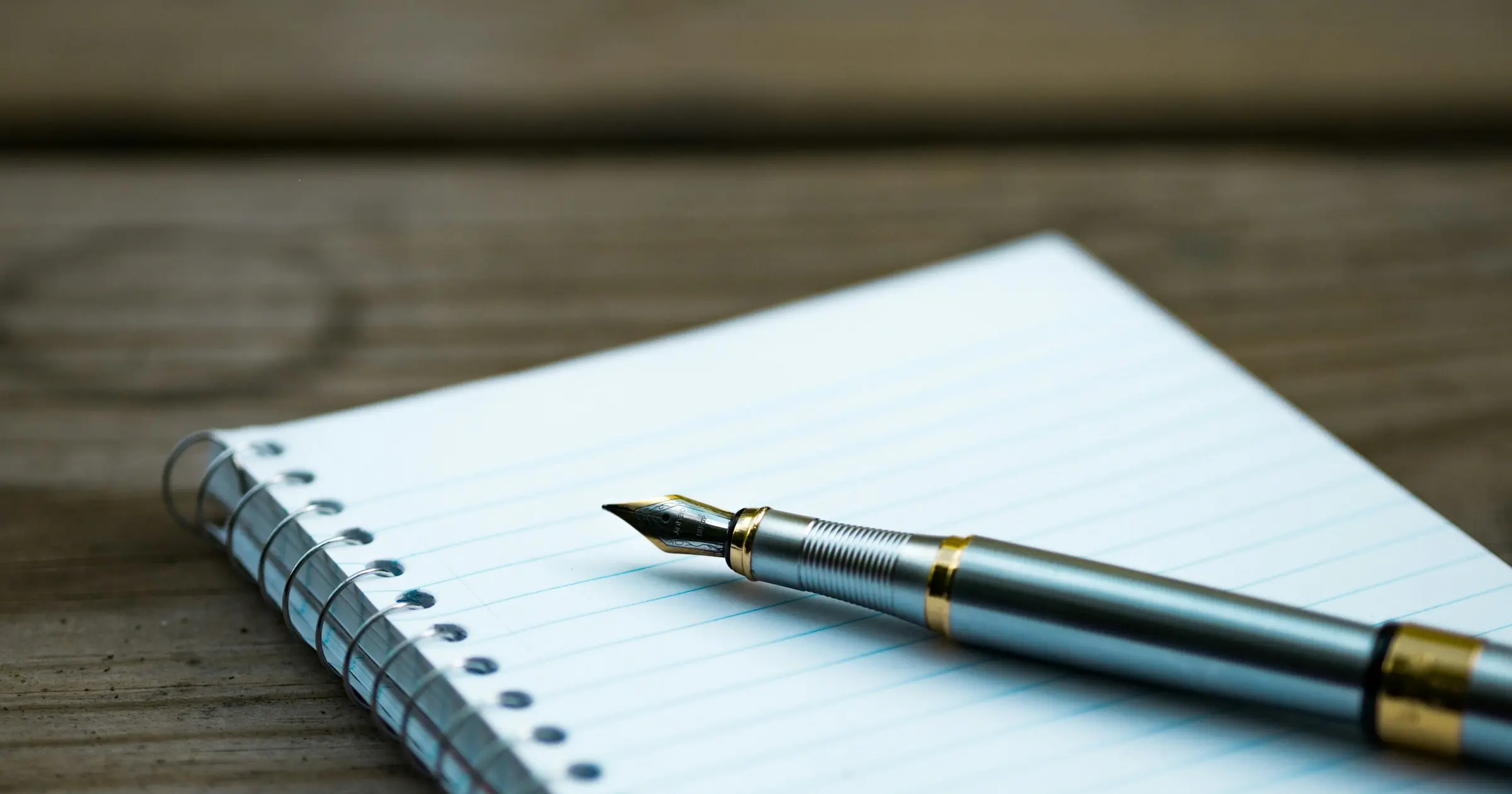 Fountain pen resting on a lined spiral notebook on a wooden table