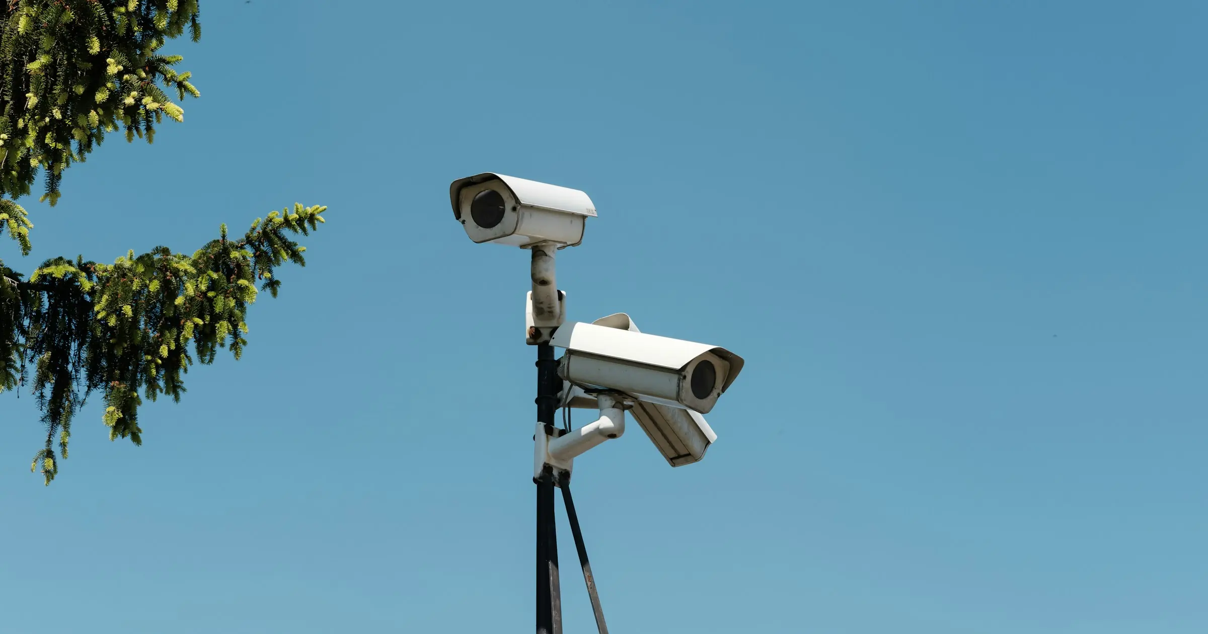 Two white security cameras on a pole against a clear blue sky