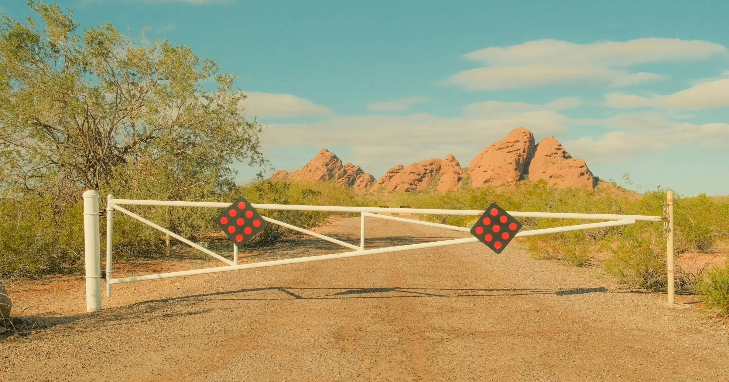 White gate closed across a dirt road leading to red desert rock formations