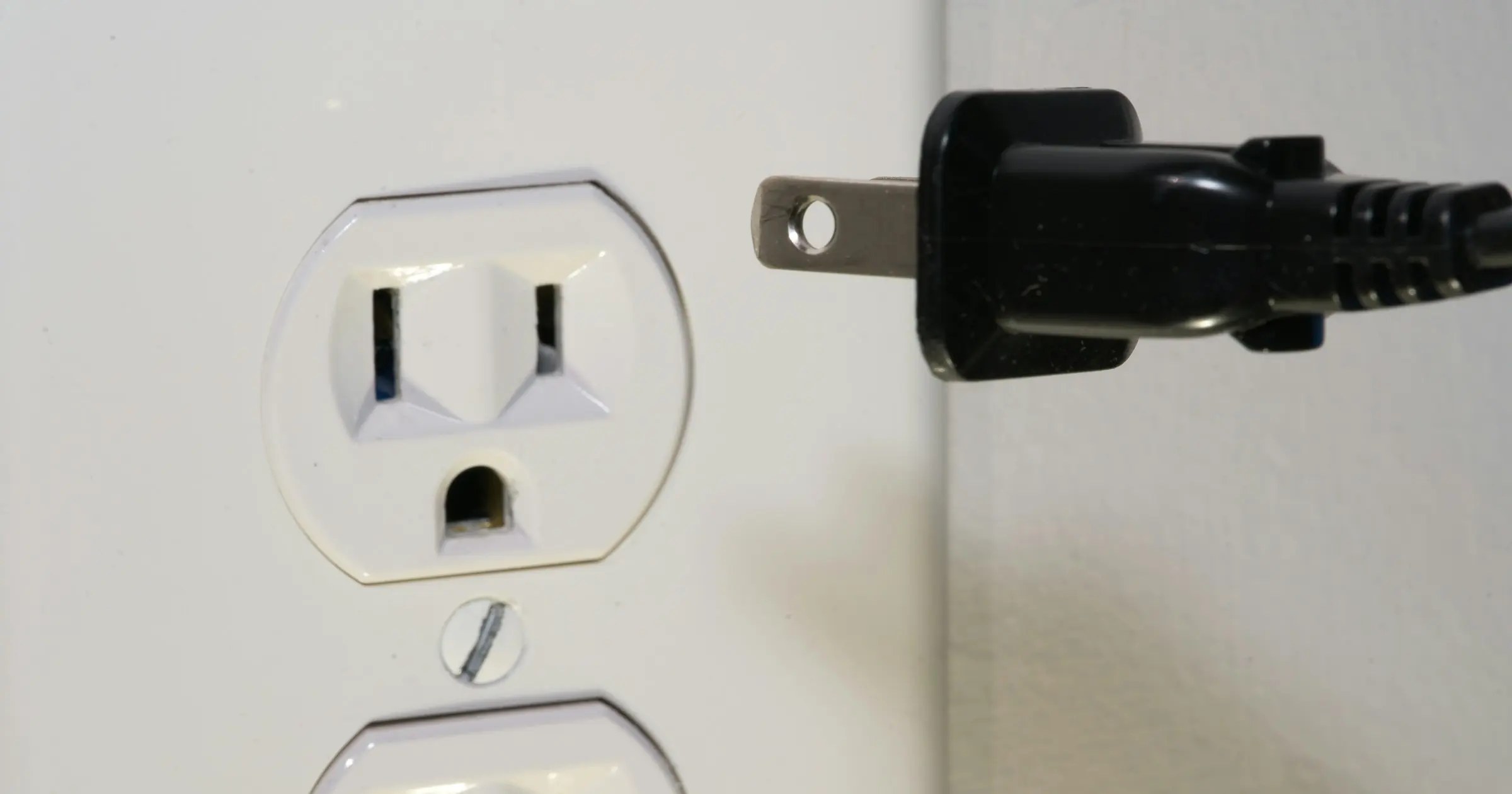 A black two-prong plug held just short of a white wall outlet