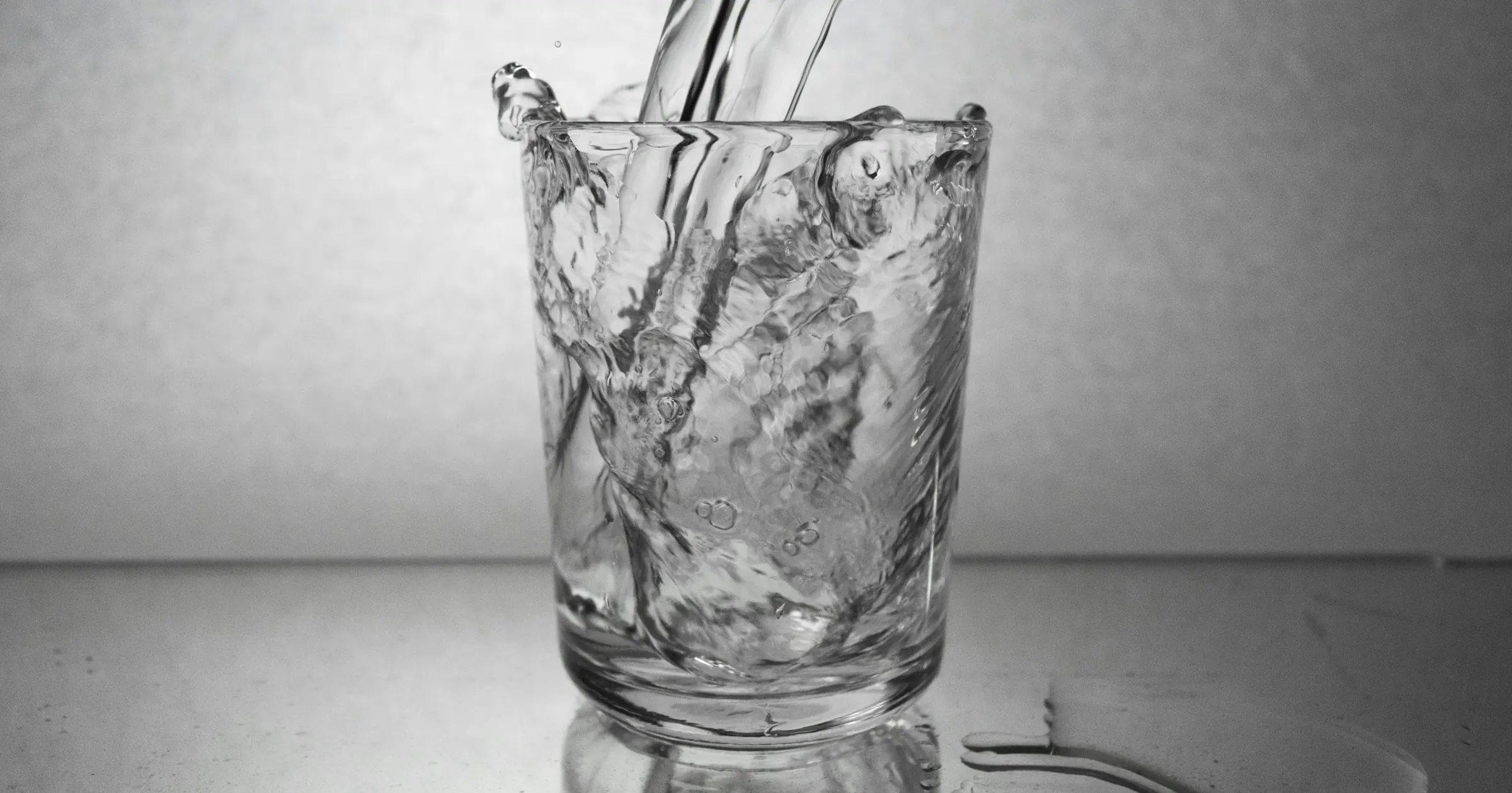Black-and-white photo of water pouring into a full glass and spilling over onto the table