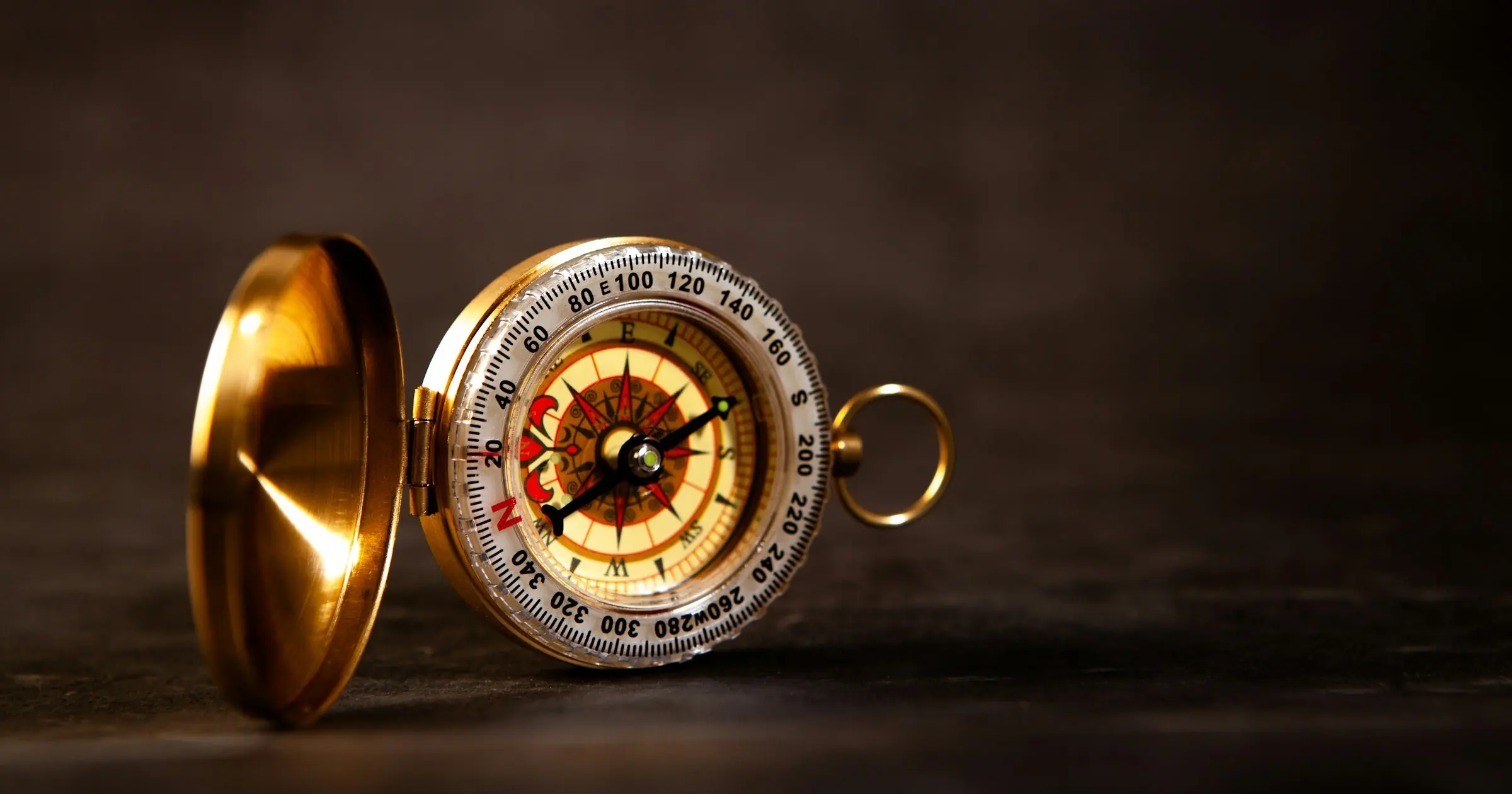 An open brass pocket compass standing on a dark surface