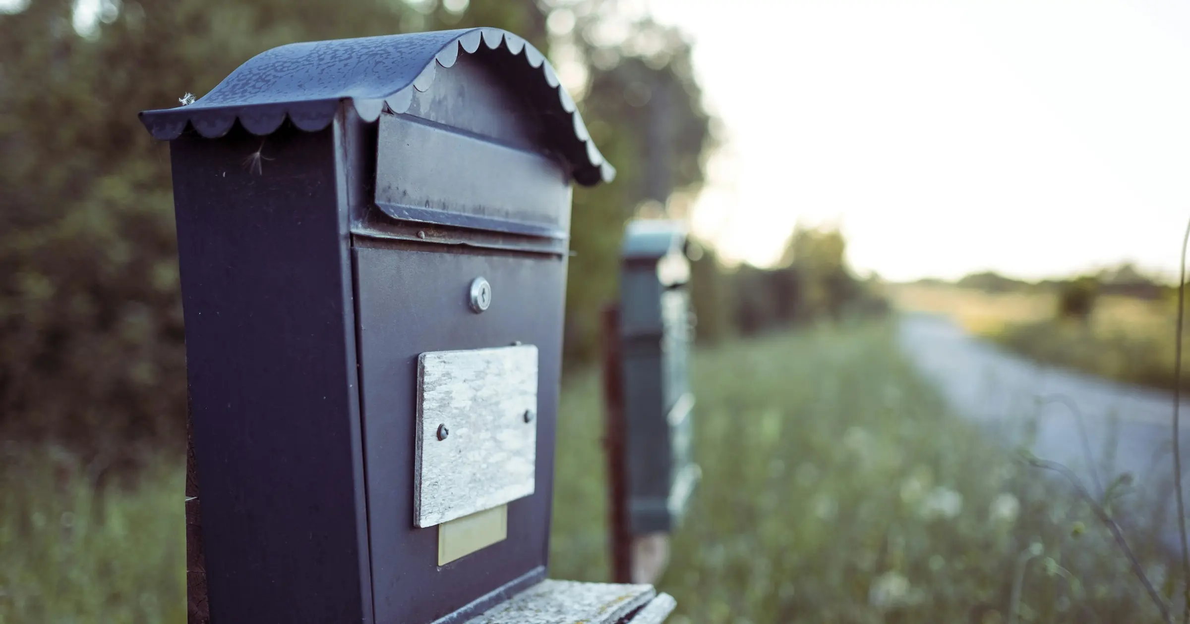 Black metal mailbox with a letter slot on a post beside a country road