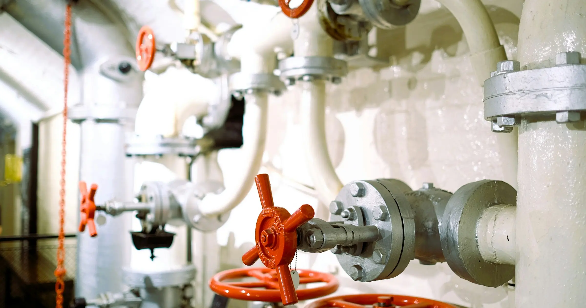 Branching white industrial pipes with red valve wheels