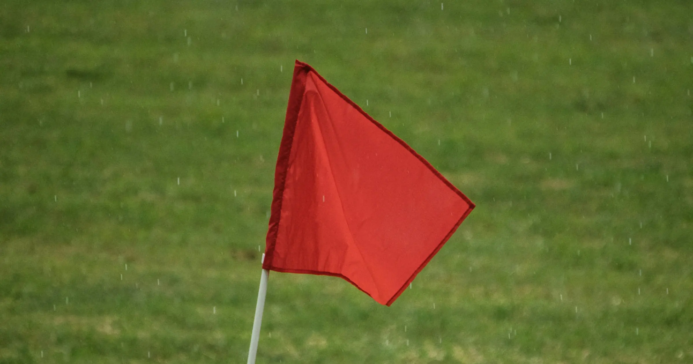 A red flag on a pole against green grass in the rain