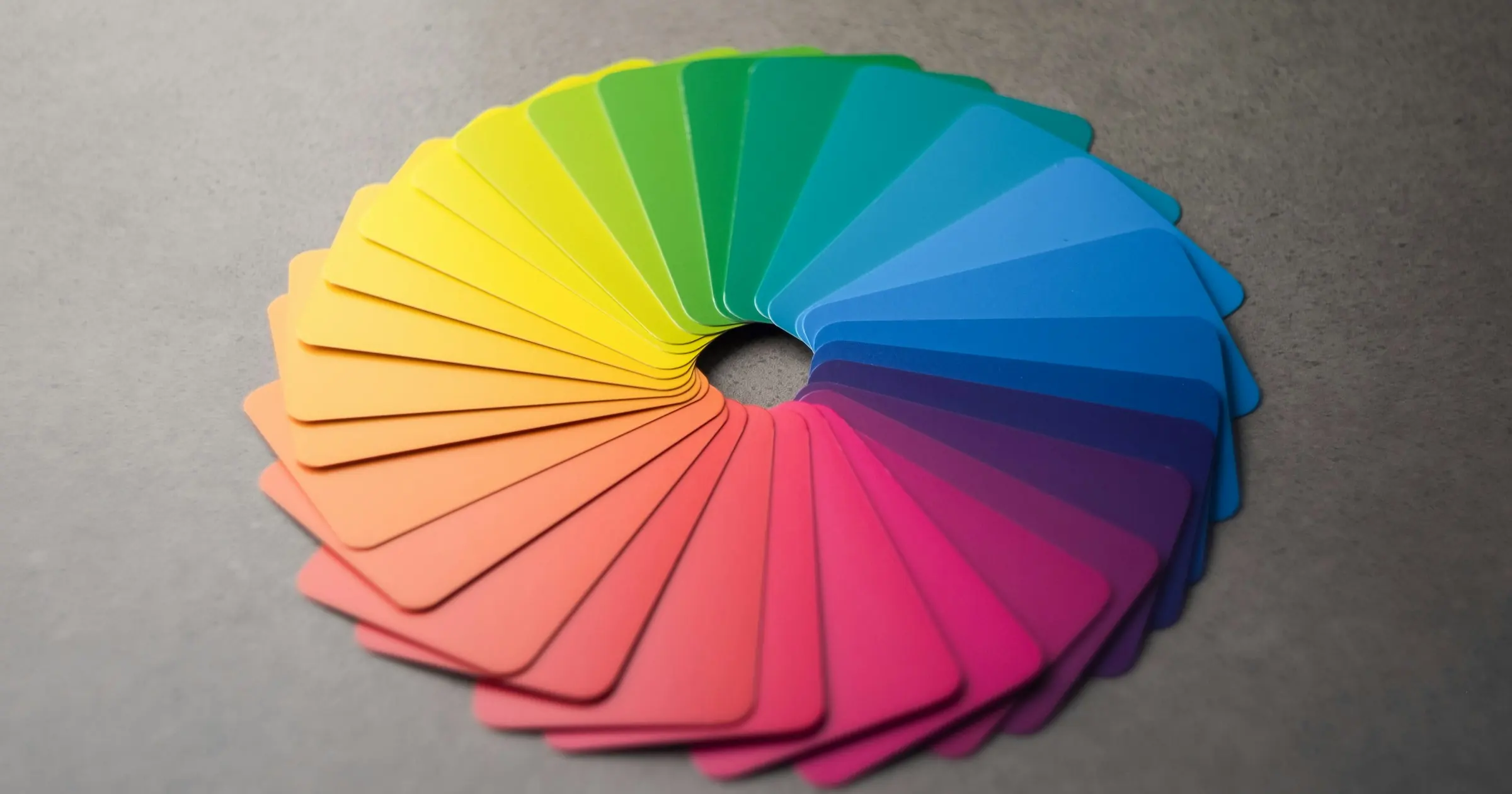 Colour swatch cards fanned into a rainbow circle on a grey surface