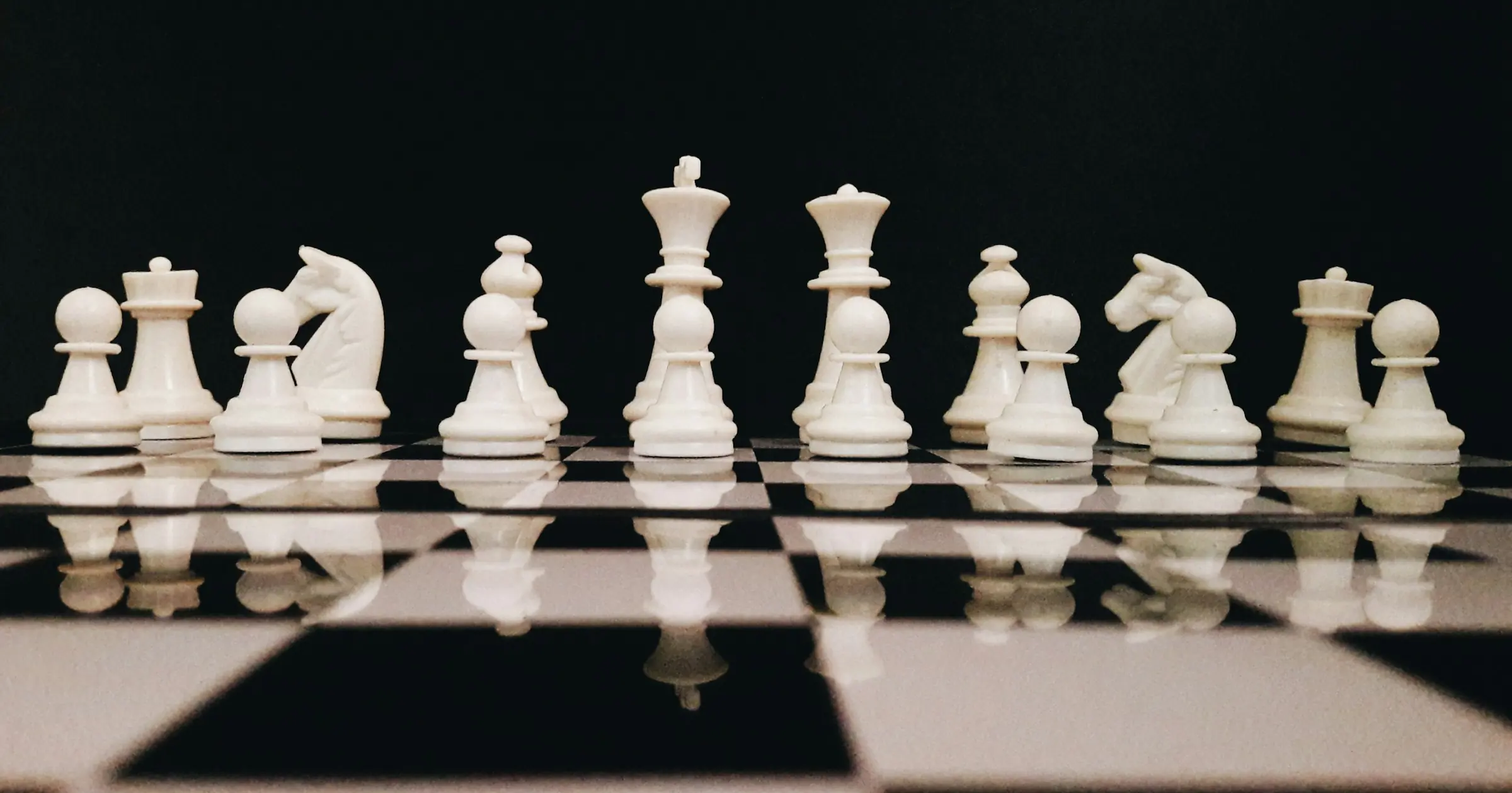 White chess pieces grouped in a line on a reflective chessboard against a black background