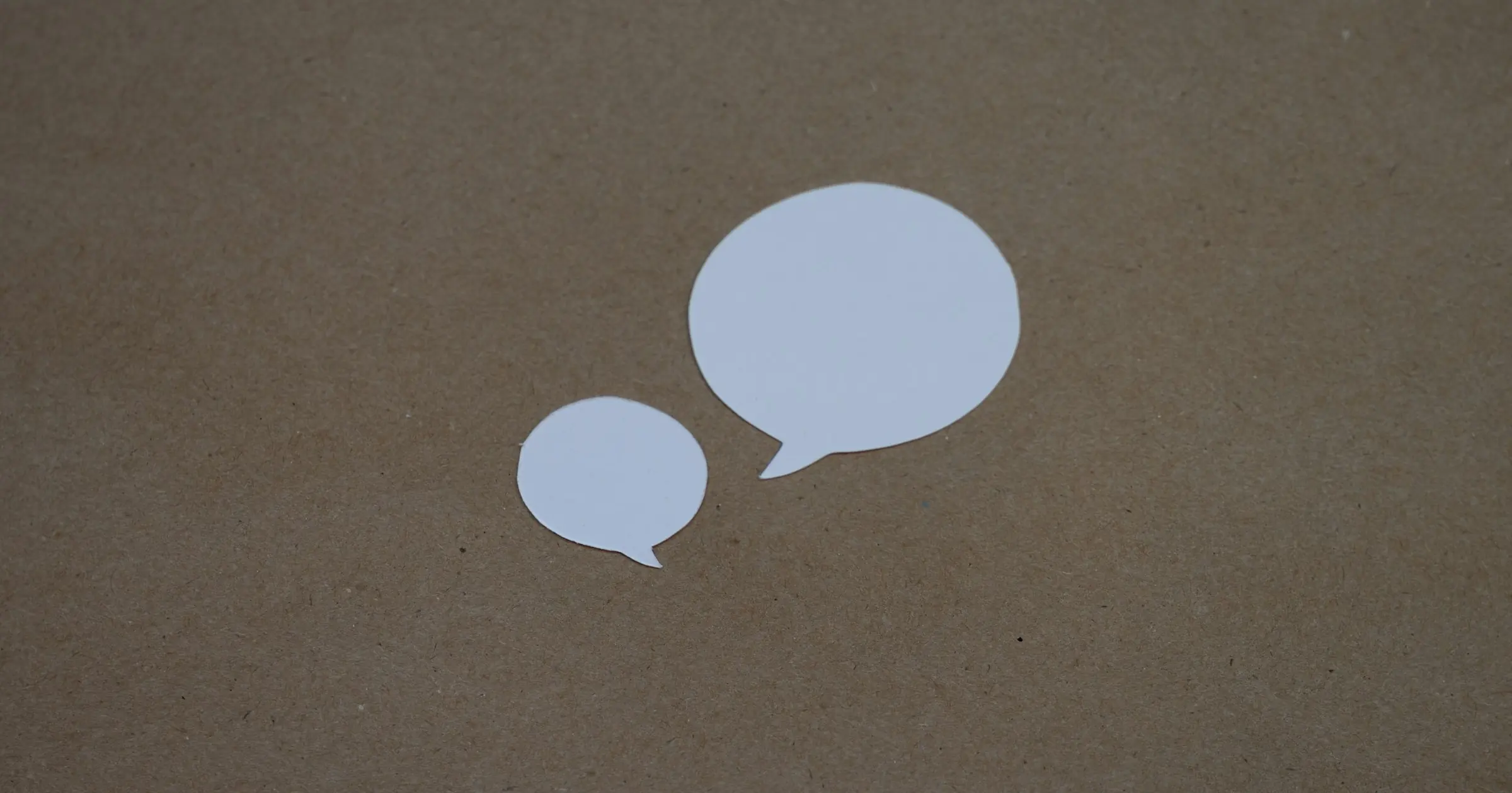 Two blank white paper speech bubbles on a brown kraft paper background