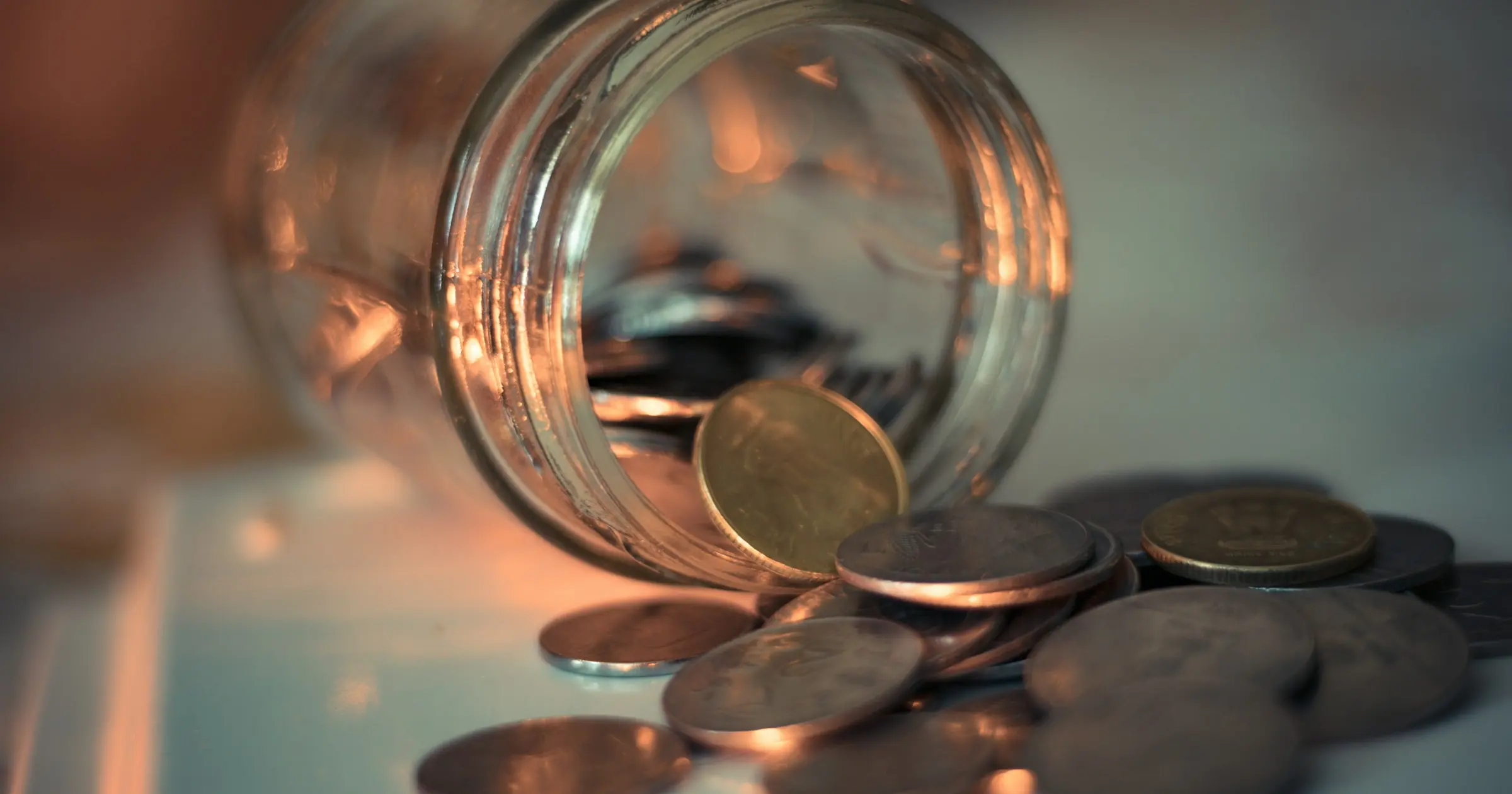 Coins spilling out of a glass jar lying on its side