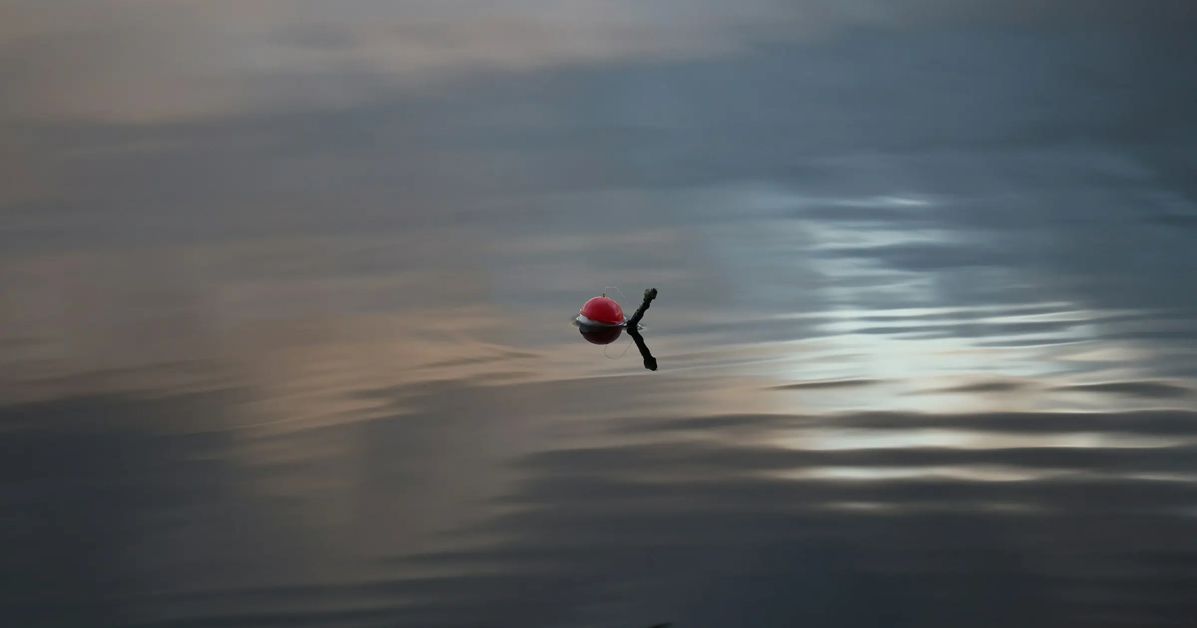 A single red fishing float on calm, still water at dusk
