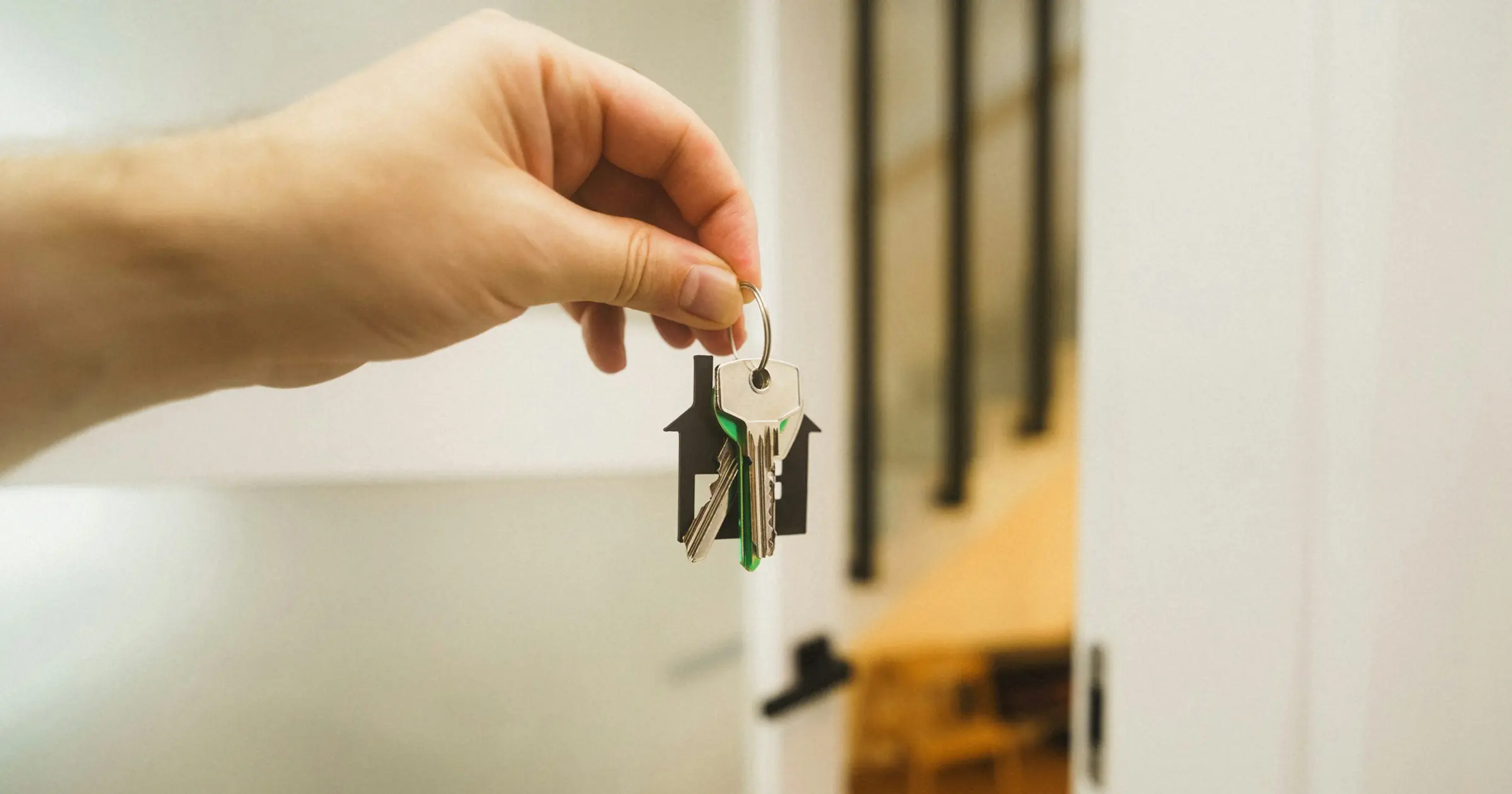 A hand holding out a set of house keys in front of an open door.