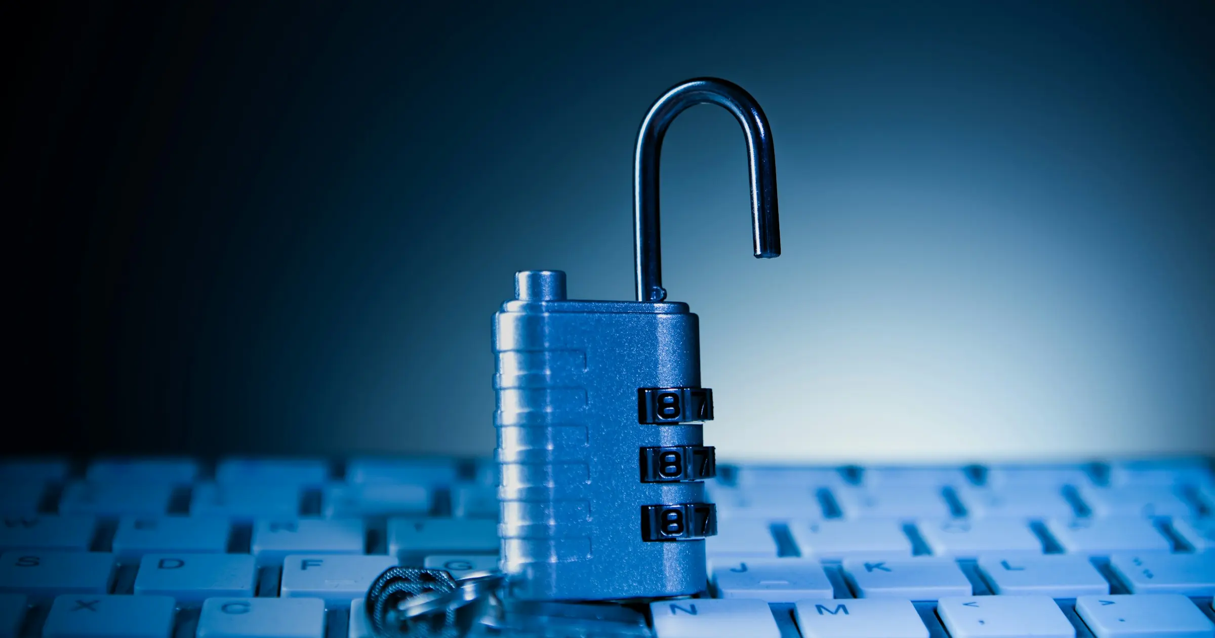 An unlocked combination padlock standing on a computer keyboard in blue light.