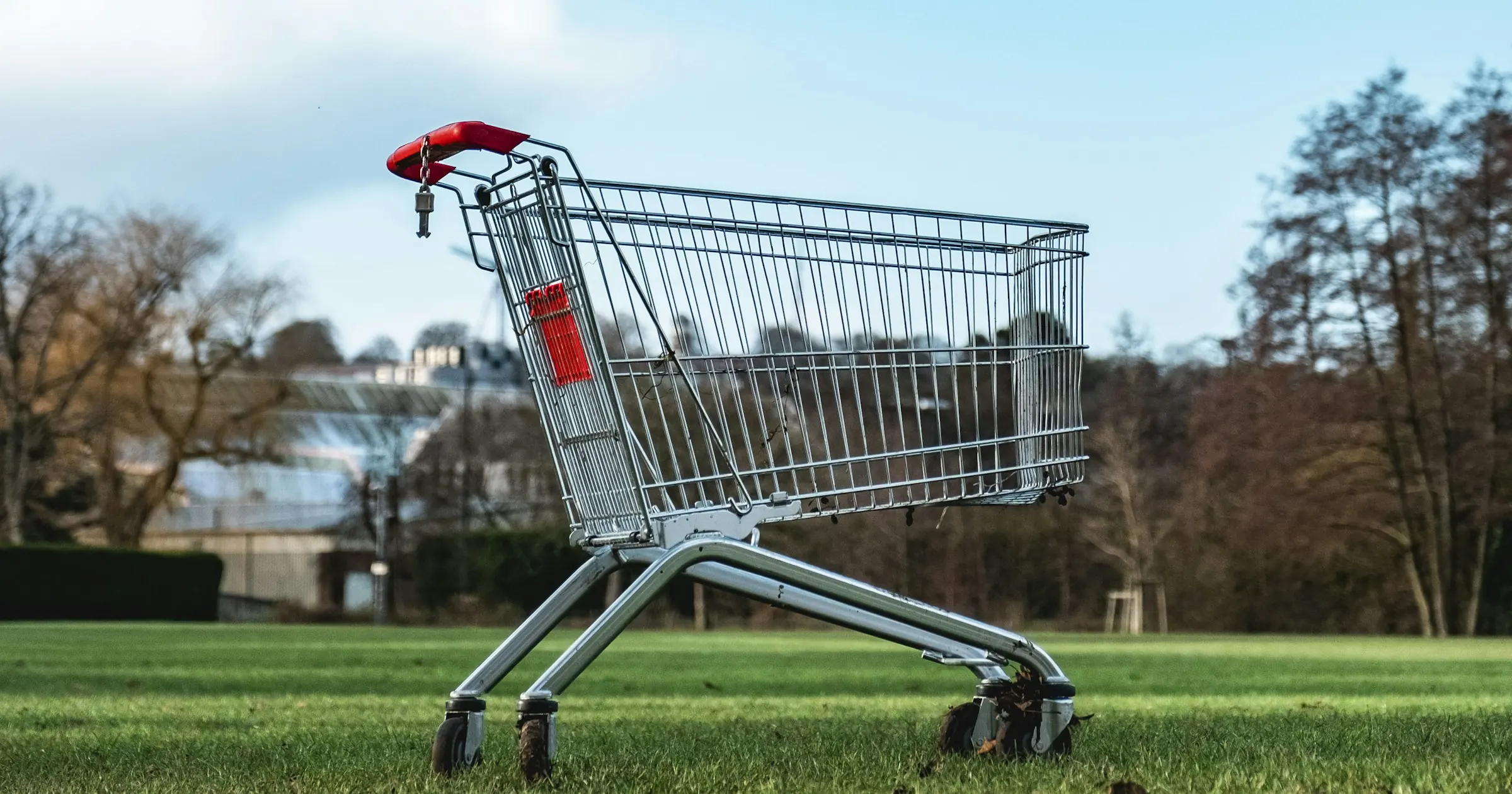 An empty shopping cart standing alone on a grass lawn