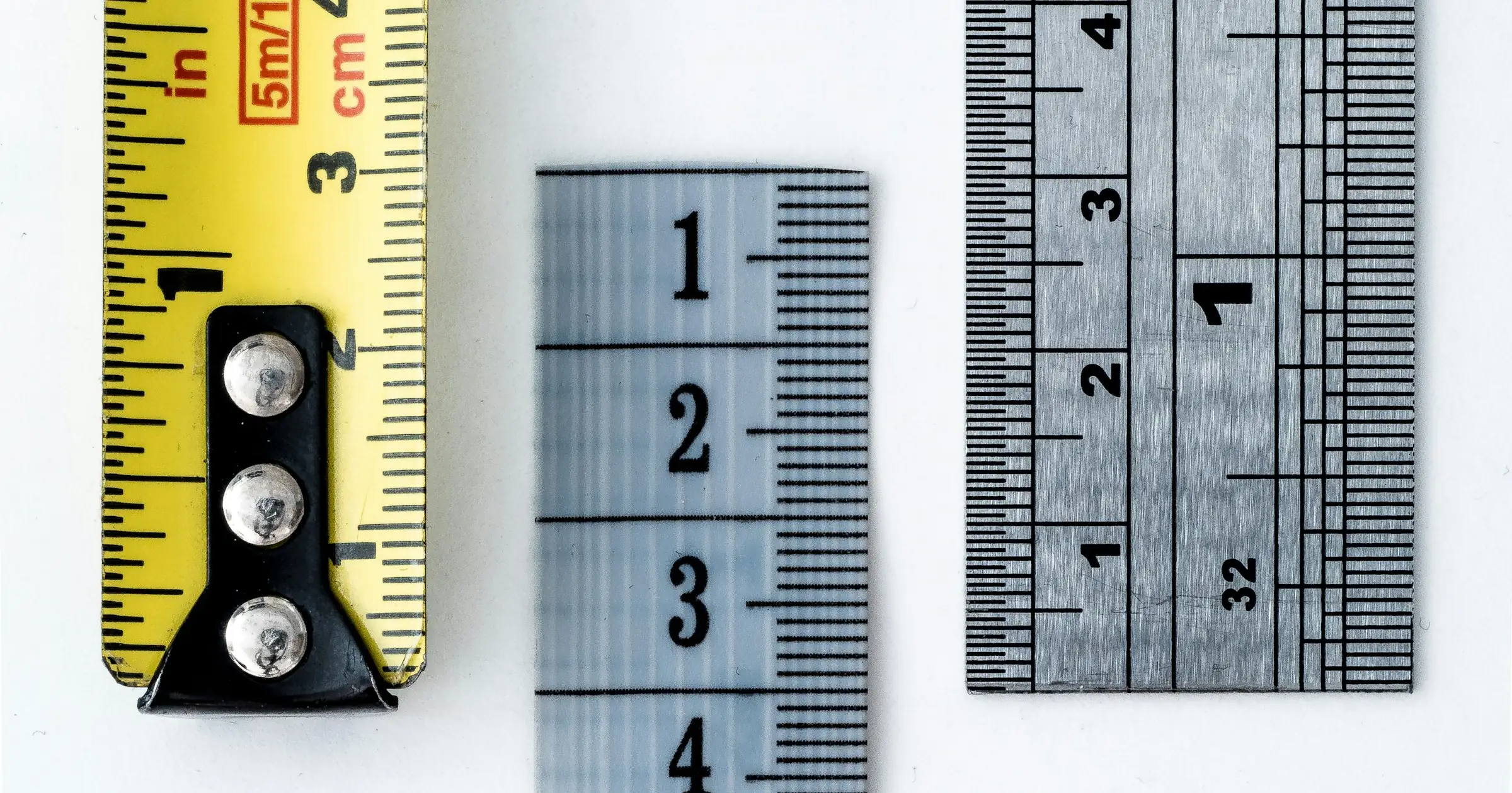 Three different measuring tapes laid side by side on a white surface.