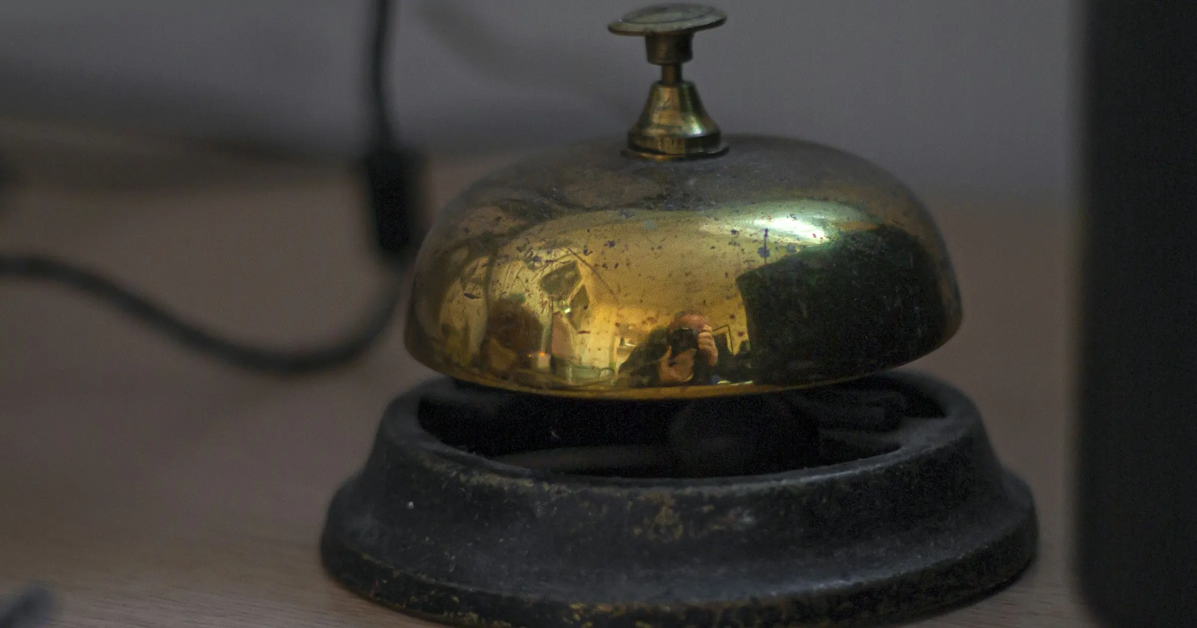 A brass service bell on a dark metal base sitting on a desk.