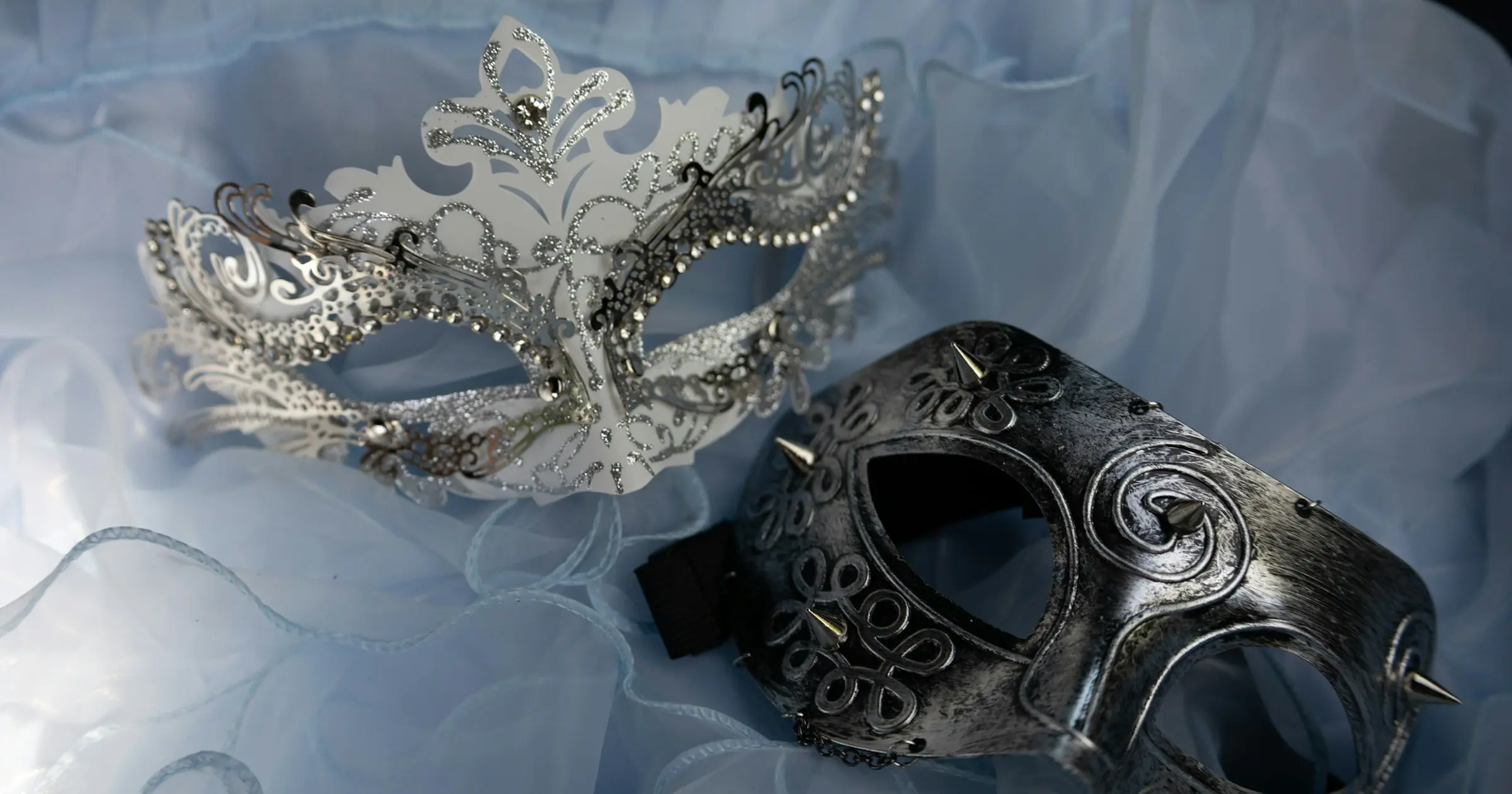 Two silver masquerade masks lying on pale blue tulle
