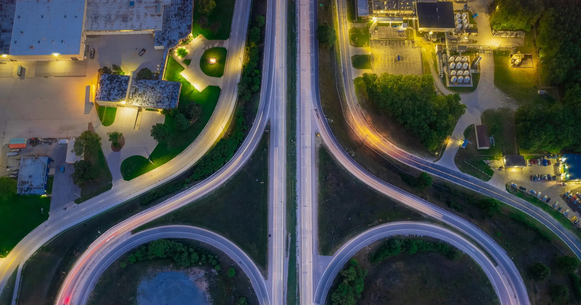 Aerial view at dusk of two curved ramps merging into a straight highway, with car light trails