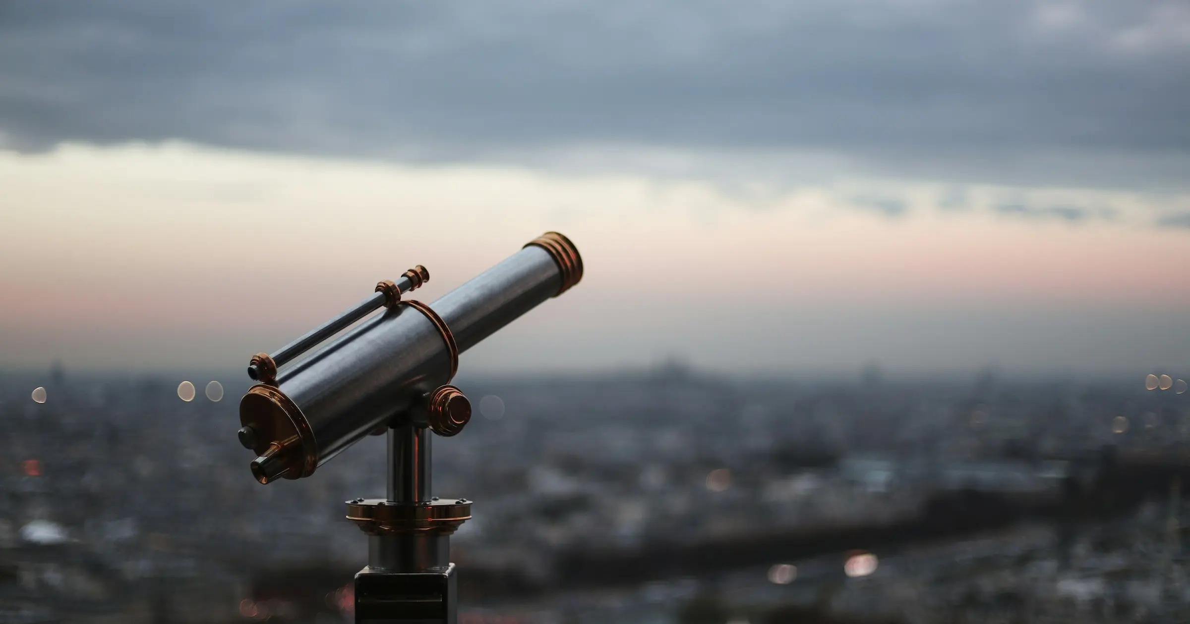 Sightseeing telescope on a railing overlooking a city at dusk