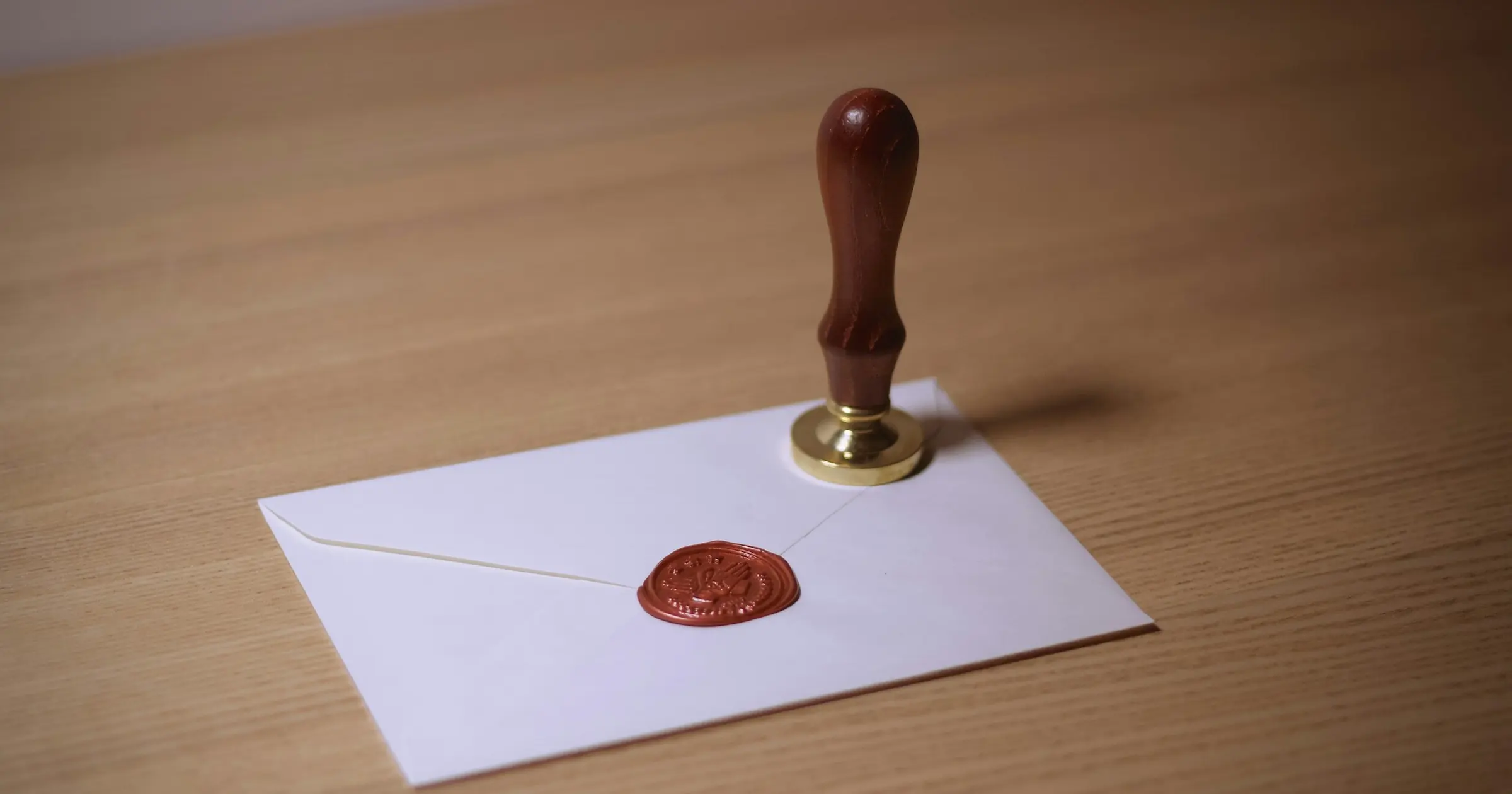 Wax seal stamp standing on a white envelope closed with a red wax seal, on a wooden desk